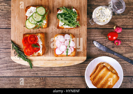 Quatre sandwiches avec des légumes frais, tomates, concombres, radis et roquette sur un fond de bois. Le beurre fait maison et pain grillé. Vue d'en haut. Banque D'Images