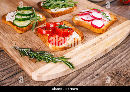 Quatre sandwiches avec des légumes frais, tomates, concombres, radis et roquette sur un fond de bois. Le beurre fait maison et toasts. focus sélectif. Banque D'Images