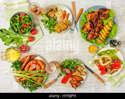 Table de dîner avec la variété de la nourriture, des ailes de poulet frites, saucisses, légumes grillés à la poêle, de la salade et de la bière sur la table en bois. Vue d'en haut. Savs copie Banque D'Images