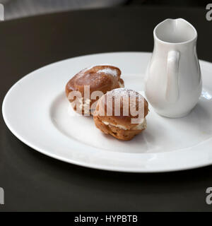 Une carafe avec du chocolat chaud et deux éclairs avec de la crème sur une plaque sur une table dans un café Banque D'Images