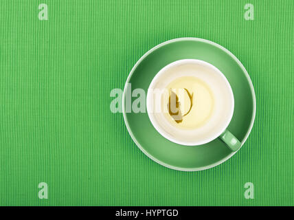 Tasse vide de thé vert clair avec la feuille sur fond vert plus de soucoupe à nappe textile, Close up, augmentation de la vue supérieure Banque D'Images