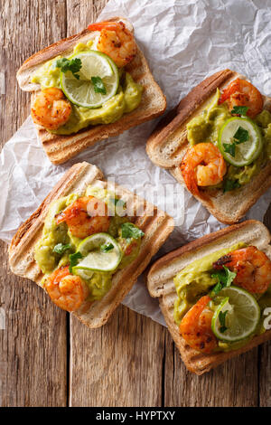 Délicieux toasts de guacamole, crevettes et lime gros plan sur la table. Vue verticale d'en haut Banque D'Images