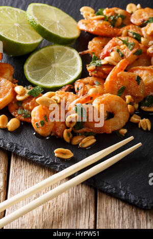 Crevettes sautées : cuisine asiatique avec des arachides, de la chaux et des verts sur la table gros plan vertical. Banque D'Images