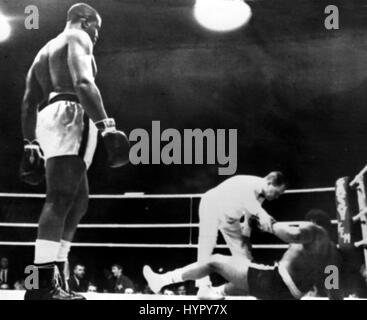 L'ancien champion du monde Sonny Liston se tient calmement, d'armes à ses côtés, comme l'arbitre aide son adversaire fellow American Dave Bailey à ses pieds après avoir été renversé et compté dans le premier tour de l'heavyweight bout tenu dans Masshallen, Göteborg, Suède. Liston a pris seulement 2 minutes 22 secondes pour disposer de Bailey. Banque D'Images