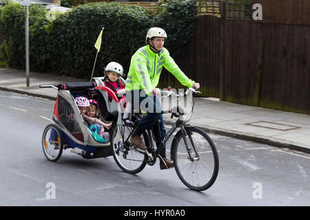 Cycliste femme sur Vélo / Vélo avec  + 3 enfants ; coopération avec siège enfant pilote casque & cycle remorquage remorque Chariot avec 2 / 2 enfants avec un casque. UK. Banque D'Images