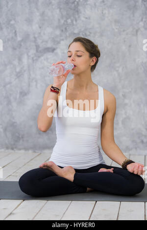 Sensation de soif. Fatigué des jeunes femmes en tenue de sport de l'eau potable et assis sur le tapis d'exercice Banque D'Images