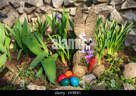 Lapin de Pâques en paille et les oeufs de pâques teints colorés dans le lit de fleur Banque D'Images