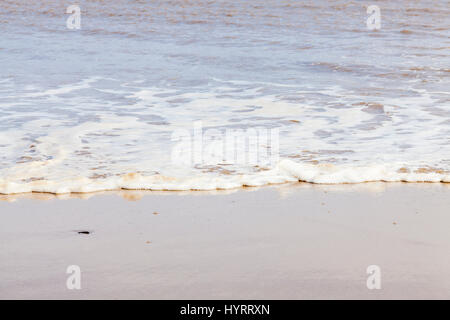Écume de mer ou spume sur la marée qui s'écoulent dans le sable d'une plage, England, UK Banque D'Images
