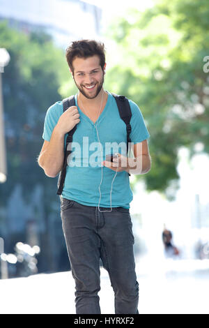 Portrait of a young man walking outdoors avec sac et téléphone mobile Banque D'Images