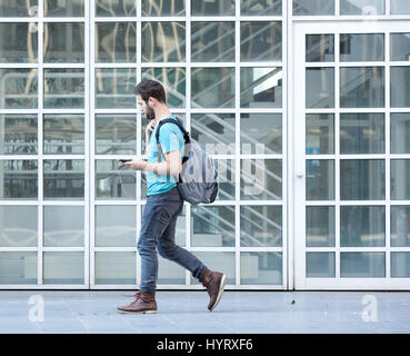 Side view portrait of a male student walking on campus avec sac et téléphone mobile Banque D'Images