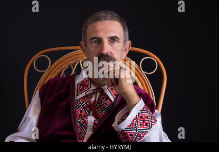 Beau portrait de l'Ukrainien pays-homme assis dans un fauteuil en osier, vêtu de vêtements traditionnels (Vyshyvanka) Banque D'Images
