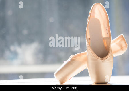 Une paire de chaussures de ballet, pointes, debout dans la lumière du soleil contre une fenêtre. Banque D'Images
