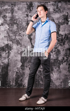 Beau jeune homme charmant dans la soirée à parler au téléphone, lwhile article, fond gris Banque D'Images
