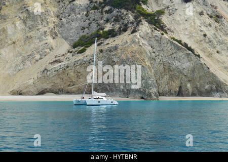 Catamaran blanc ancrée dans le calme près de la mer turquoise et la plage de sable de falaises verticales Banque D'Images