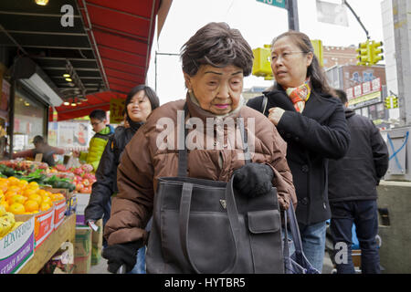 Une vieille femme chinoise à l'extérieur des magasins un jour froid sur Main Street dans le quartier chinois, le rinçage, Queens, New York City Banque D'Images