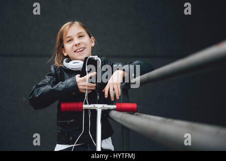 Girl wearing Blouson cuir noir et blanc un casque sur le scooter et permanent à l'aide de smart phone piscine Banque D'Images