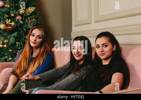 Trois belles jeunes copines sur un canapé près de l'arbre de Noël. Studio portrait horizontal. Banque D'Images