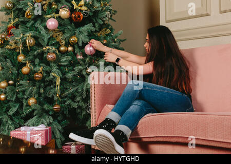 Belle jeune femme brune sur un canapé décore arbre de Noël. Studio portrait horizontal. Banque D'Images