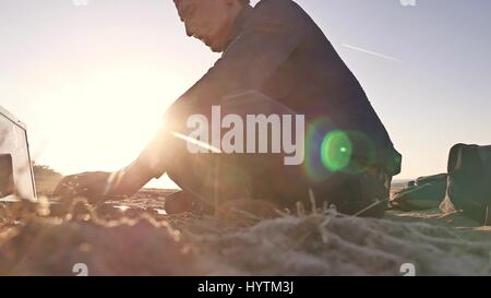 Freelancer. Silhouette homme travaillant sur ordinateur portable freelancer assis sur le sable le soleil coucher de soleil Banque D'Images