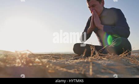 La religion. Homme qui prie assis sur le sol au coucher de soleil religion silhouette Banque D'Images