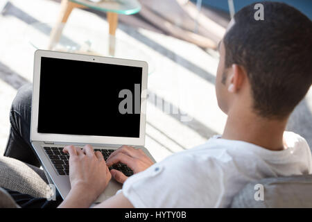 Vue arrière du jeune homme noir incognito en t-shirt blanc assis à l'intérieur et en tapant sur son ordinateur portable Banque D'Images