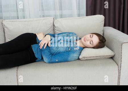 Belle femme en pantalon noir et une chemise bleue dormir sur un canapé. Banque D'Images