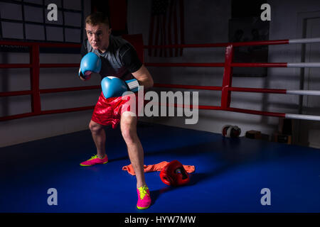 Young male boxer dans des gants de boxe se lève et se prépare pour la bataille dans les ring de boxe dans une salle de sport Banque D'Images