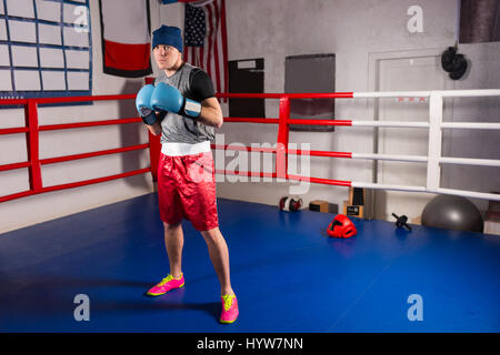 Young male boxer dans des gants de boxe se prépare pour la bataille dans les ring de boxe dans une salle de sport Banque D'Images