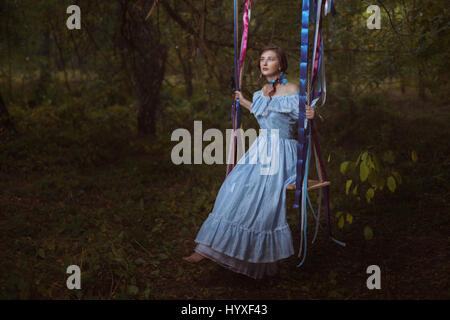 Femme rétro fabuleux dans une tenue correcte dans les bois assis sur une balançoire. Banque D'Images