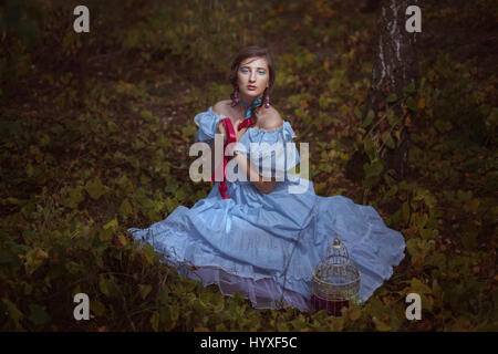 Young Girl en tenue rétro assis sur l'herbe dans la forêt. Banque D'Images