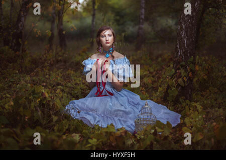 Jeune fille avec ruban rouge dans les mains assis sur l'herbe dans la forêt. Banque D'Images