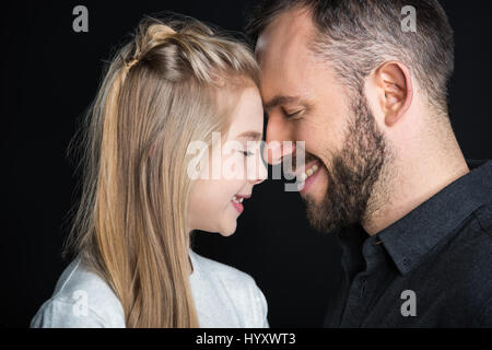 Jeune père et sa petite fille de toucher leur front et souriant sur noir Banque D'Images