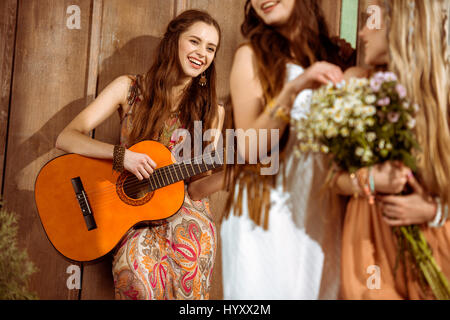 Young smiling woman playing guitar et la regardant amis féminins Banque D'Images