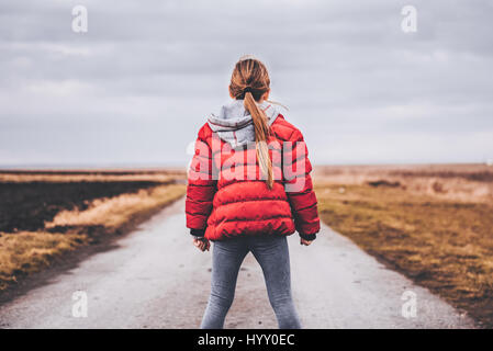 Girl wearing red jacket debout seul sur la route et à la recherche à distance Banque D'Images