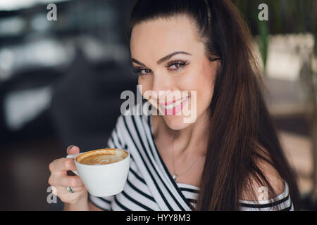 Un close-up portrait d'une femme avec un sourire parfait avec une tasse de cappuccino ou de café. Les dents blanches et le maquillage. Banque D'Images