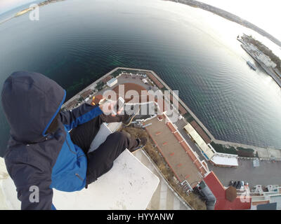 SEVASTOPOL, UKRAINE : UN Adrenaline Junkie a risqué sa vie après l'ascension d'une 195 pieds de haut monument aux héros de guerre russe WW2 juste pour obtenir une nouvelle vidéo de la ville ci-dessous. Vertigo-induisant des images et séquences vidéo montrent le grimpeur audacieux s'emmitoufler d'une échelle à l'intérieur de la spire avant de sortir sur une surface qui est incliné à 45 degrés, sans aucun équipement de sécurité. Le rooftopper promenades le long de la surface inclinée jusqu'à ce qu'il atteint le bord où il est assis et balance ses jambes tout en passant des messages sur son téléphone. C'est le vidéo a été filmé au sommet de l'Obélisque d'Bayonet-Sail Sevastopo dans Banque D'Images