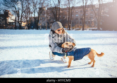 Woman Petting Dog wearing son manteau d'hiver dans la neige Banque D'Images