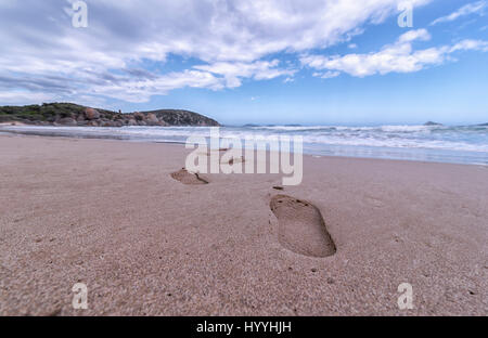 Un portrait d'une plage de sable avec des empreintes de pieds menant vers les vagues avec un ciel bleu menant vers l'horizon. Ici, dans l'horizon. Banque D'Images