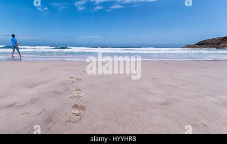 Un portrait d'une plage de sable avec des empreintes de pieds menant vers les vagues avec un ciel bleu menant vers l'horizon. Ici, dans l'horizon. Banque D'Images