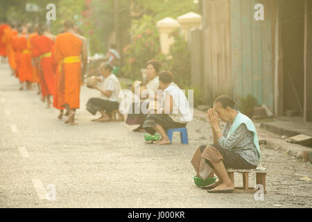 République démocratique populaire du Laos, Laos, Luang Prabang - 20 juin : femme prie après l'aumône aux moines bouddhistes dans la rue, Luang Prabang. Banque D'Images