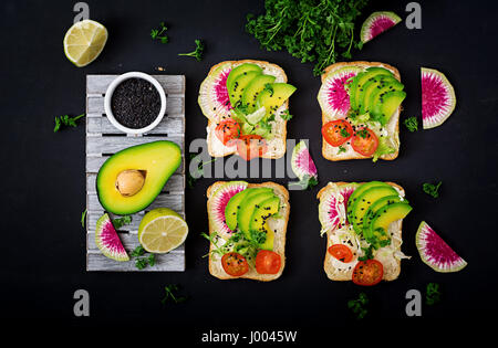 Sandwiches vegan avec avocat, radis pastèque et les tomates sur un fond noir. Mise à plat. Vue d'en haut Banque D'Images