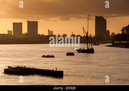 Tamise barge traditionnelle voile bateaux sont silhouette sur le coucher du soleil à Greenwich, avec des immeubles à appartements et les blocs de bureau derrière. Banque D'Images