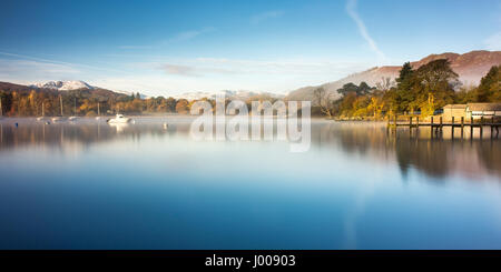 La brume s'élève des eaux calmes du lac Windermere, à Ambleside Pier, à côté de l'automne et forestiers dans le cadre de montagnes enneigées en Angleterre du Lake District. Banque D'Images