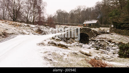 Neige de l'hiver se trouve sur le pittoresque pont voûte en pierre et grange traditionnelle à Ashness dans les bois au-dessus de la Derwent Water Lake District Banque D'Images