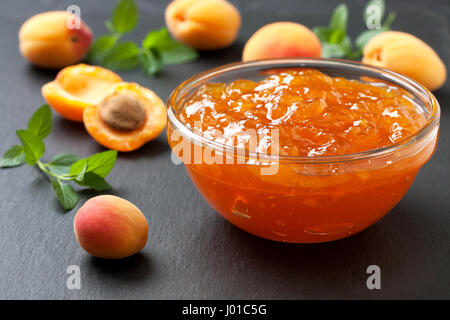 Confiture d'abricot dans un bol en verre , abricots frais sur fond d'ardoise noire Banque D'Images