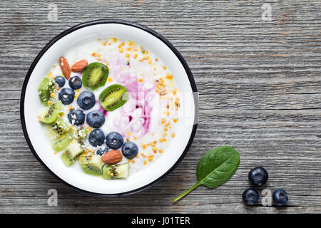 Bol à smoothie aux bleuets, kiwi, amandes, noix de coco, les graines de chia et pollen. Vue de dessus, l'arrière-plan en bois rustique, copy space Banque D'Images
