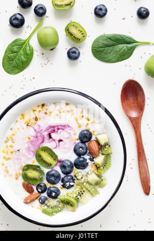 Bol à smoothie acai, kiwi, bleuets, amandes, noix de coco, du pollen d'abeille et bébés épinards sur fond blanc. Vue de dessus de désintoxication sain smoothy Banque D'Images