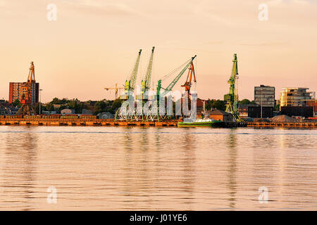 Grues et navires en mer Baltique au port de Klaipeda, Lituanie. Au coucher du soleil Banque D'Images