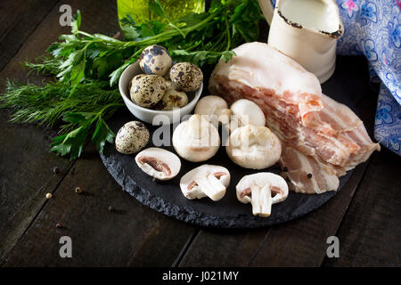 Culinaire - sur un fond d'ardoise champignons, jambon, lait et oeufs de cailles. Des ingrédients frais pour faire une omelette. Copier l'espace. Banque D'Images