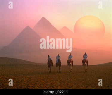 Quatre coureurs de chameau, les Pyramides et le soleil levant, Giza, Le Caire, Egypte Banque D'Images